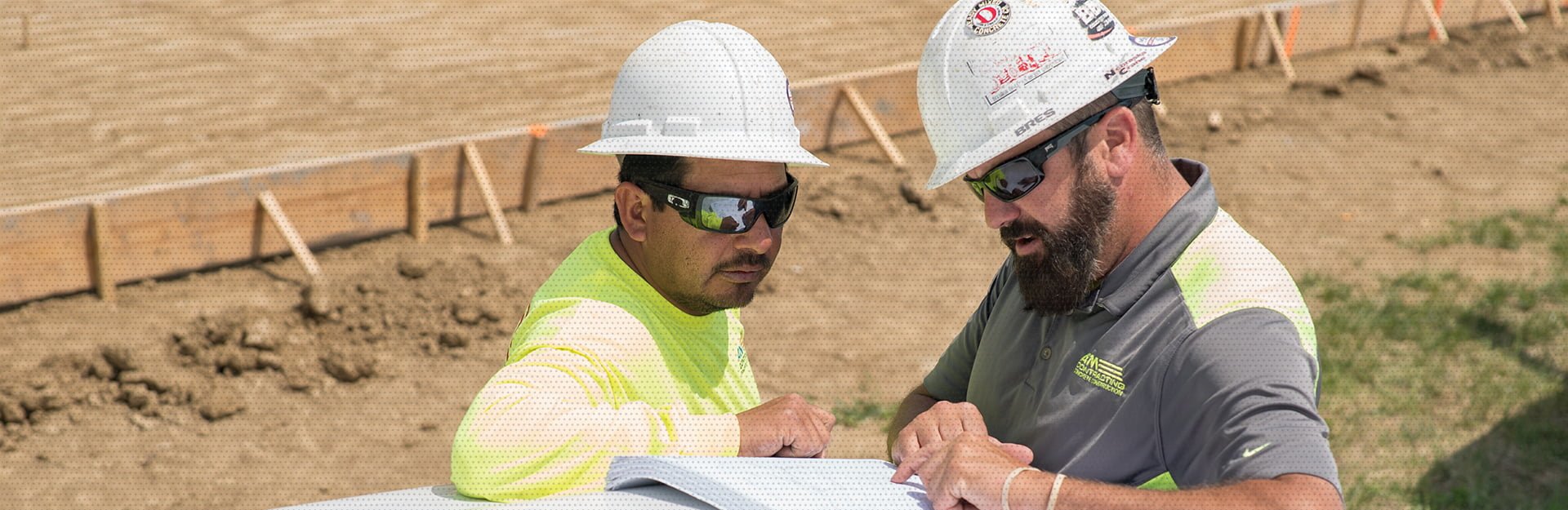 The AM Contracting guys reading the specs for their new job site analyzing and focusing on the details along with a wooden structure in the background to keep the new concrete in place.