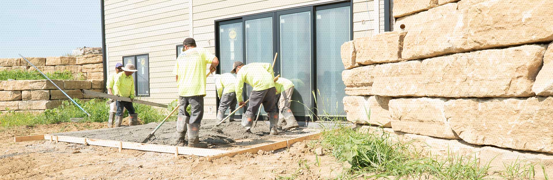 A crew of AM Contracting employees working on a new patio porch for a residential client as wet cement is being shifted around inside a wooden barrier.