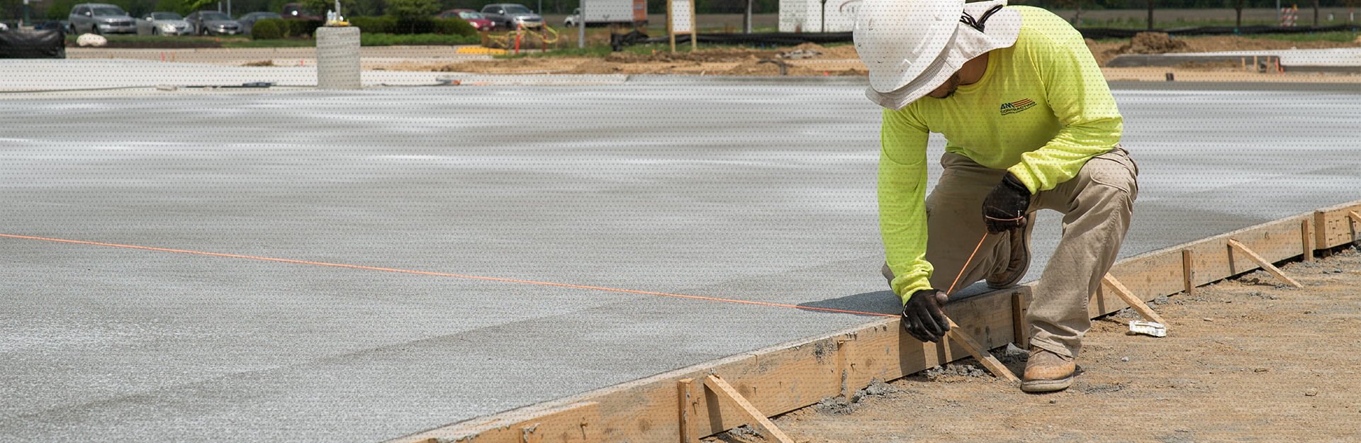 An AM Contracting employee measuring concrete as he rests on a wooden concrete barrier